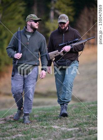 Two men hunting with rifles in camouflage walking through a forest clearing 138047869