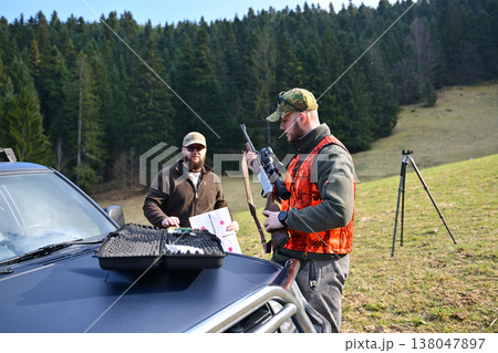 Hunters preparing rifle and targets beside a pickup truck on a forested hillside shooting range 138047897