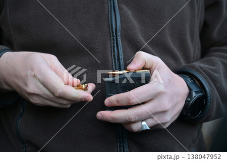 Man loading rifle magazine with bullets outdoors, close-up of hands handling ammunition 138047952