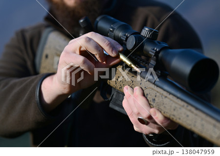 Hunter loading a scoped bolt-action rifle with a cartridge during outdoor hunting preparation Hunter loading a scoped bolt-action rifle with a cartridge during outdoor hunting preparation 138047959