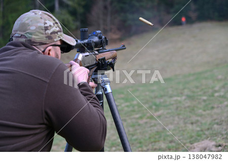 Man shooting a scoped rifle on a tripod during outdoor target practice in a grassy field Man shooting a scoped rifle on a tripod during outdoor target practice in a grassy field 138047982