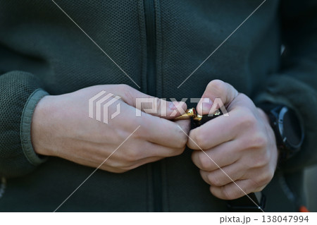 Man is hands loading a brass bullet into a pistol magazine close up with green jacket and watch 138047994