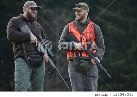 Two hunters walking and laughing in a forest wearing blaze orange vest and camouflage gear Two hunters walking and laughing in a forest wearing blaze orange vest and camouflage gear 138048010
