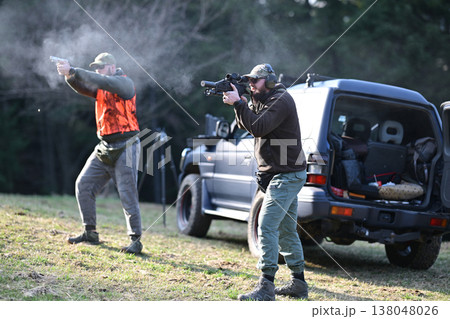 Two men firing rifles and handguns near SUV during outdoor tactical shooting training exercise 138048026