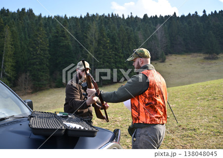 Hunters preparing rifle and gear outdoors near forest edge before a day of hunting 138048045