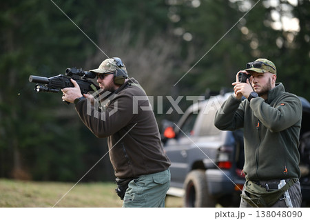 Two men practicing rifle shooting and tactical training outdoors with ear protection and optics 138048090