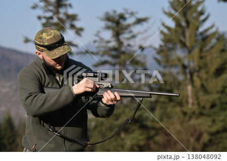 Hunter adjusting rifle scope while preparing for hunting in forested mountain landscape 138048092
