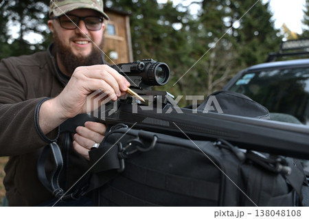 Hunter loading a rifle with a bullet at an outdoor hunting spot with scope and gear 138048108