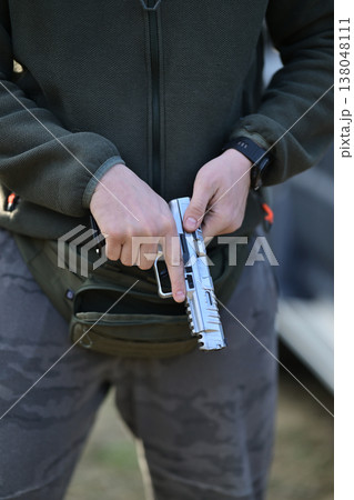 Person handling a handgun pistol with careful grip and safety in casual outdoor setting 138048111