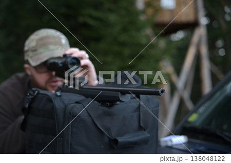 Hunter aiming a scoped rifle from a rest bag during outdoor hunting and target practice in forest 138048122