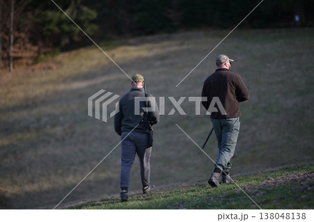 Two hunters walking across a grassy field carrying rifles on a cool overcast day 138048138