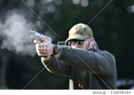 Shooter firing a handgun at an outdoor range with visible muzzle smoke and tactical gear Shooter firing a handgun at an outdoor range with visible muzzle smoke and tactical gear 138048184