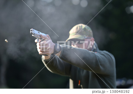 Man shooting a pistol at an outdoor range, firing a handgun during target practice 138048192