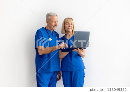 Senior male and female doctors in medical scrubs reviewing information on laptop Senior male and female doctors in medical scrubs reviewing information on laptop 138049322