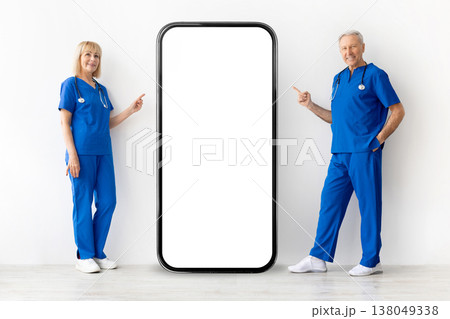 Two experienced doctors standing beside smartphone mockup and pointing at blank screen 138049338