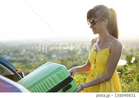 Young woman packing green suitcase in her car trunk. Travel and vacations concept. 138049831