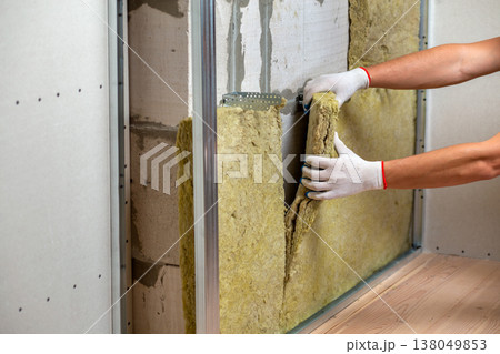 Worker insulating a room wall with mineral rock wool thermal insulation. 138049853