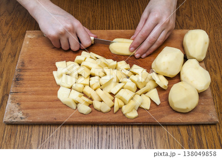 Woman's hand with a knife cutting slicing potatoes on wooden board in kitchen. Healthy eating and lifestyle. View from above close-up Woman's hand with a knife cutting slicing potatoes on wooden board in kitchen. Healthy eating and lifestyle. View from above close-up 138049858