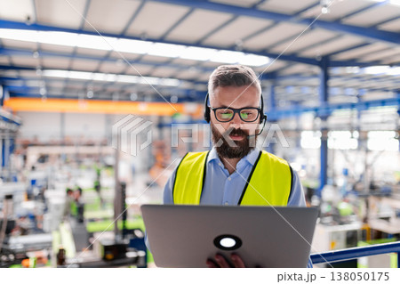 Quality manager with headset and laptop standing in industrial factory. Quality manager with headset and laptop standing in industrial factory. 138050175
