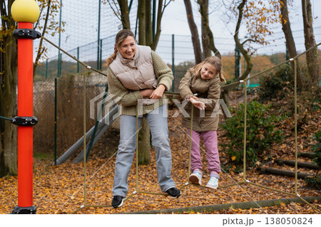 Mother balancing with daughter on rope bridge at playground autumn 138050824