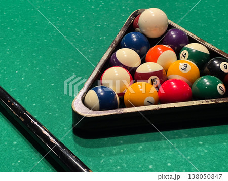 Billiard balls sit in a triangle on the green table, ready for players to start the game. Cue stick rests nearby Billiard balls sit in a triangle on the green table, ready for players to start the game. Cue stick rests nearby 138050847