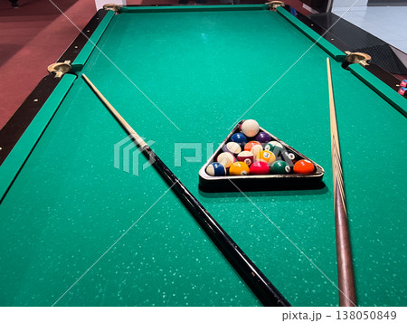 Billiard table is set up with a triangle of balls and cues positioned on either side for an upcoming game in a game room 138050849