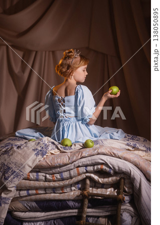 Little girl in blue dress with crown holding apple on mattresses, princess and the pea 138050895