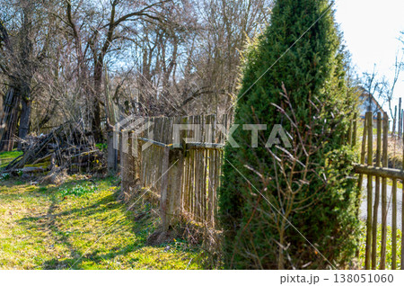 Old wooden fence leading through rural garden with sunlight and trees, peaceful countryside scene, concept of direction, boundary, journey and traditional lifestyle 138051060