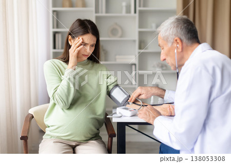 Pregnant woman experiencing dizziness while doctor checks blood pressure during prenatal consultation 138053308