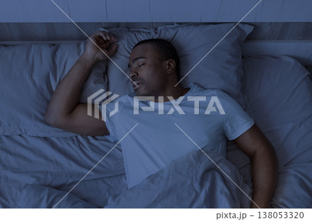 Young african american man sleeping in bed at night under blanket 138053320