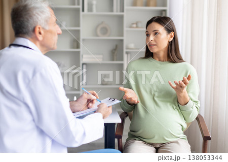 Pregnant woman explaining symptoms to doctor during prenatal consultation in clinic Pregnant woman explaining symptoms to doctor during prenatal consultation in clinic 138053344