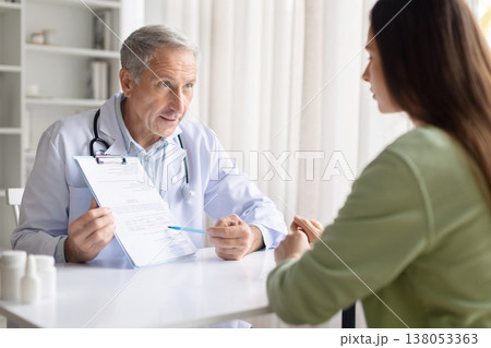 Senior male doctor showing medical document to female patient in clinic Senior male doctor showing medical document to female patient in clinic 138053363