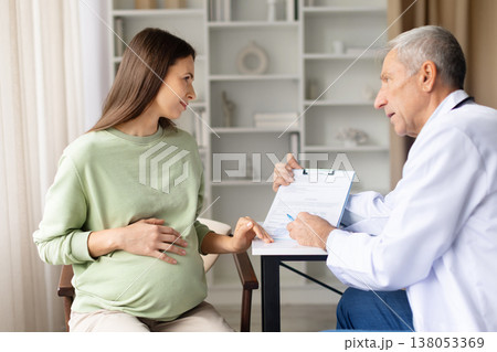 Doctor explaining prenatal medical report to pregnant patient during clinic consultation Doctor explaining prenatal medical report to pregnant patient during clinic consultation 138053369