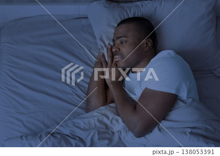 Young african american man lying in bed at night awake and thinking Young african american man lying in bed at night awake and thinking 138053391