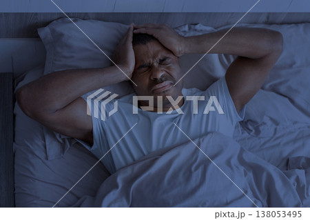 Young black man lying in bed at night holding head in pain 138053495