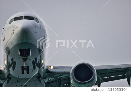 Low Angle Close-Up of a Commercial Passenger Airplane: Detailed View of the Aircraft Nose, Cockpit Windows, and a Jet Engine against a Grey Overcast Sky, Aviation and Travel Concept 138053504