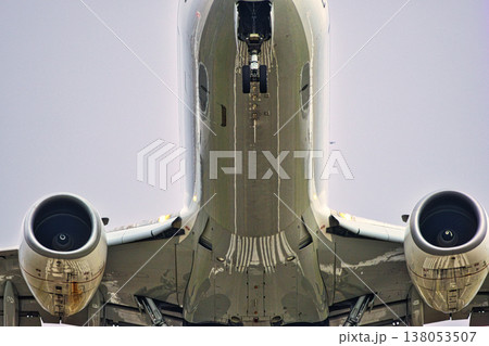 Detailed Underside View of Commercial Aircraft on Final Approach: Close-up of Jet Engines, Extended Nose Landing Gear, and Reflective Fuselage Surface against Overcast Sky 138053507