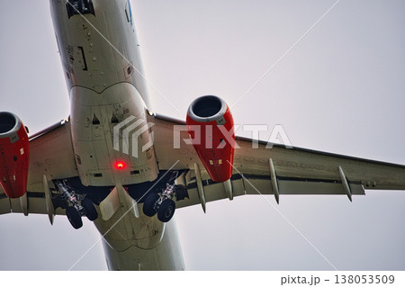 Underneath View of a Commercial Jet in Flight: Detailed Shot of Aircraft Underside, Red Jet Engines, and Extended Landing Gear against a Clear Sky, Aviation Engineering and Travel 138053509