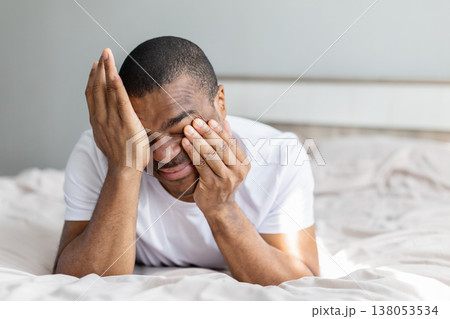 Young african american man rubbing eyes while lying on bed Young african american man rubbing eyes while lying on bed 138053534