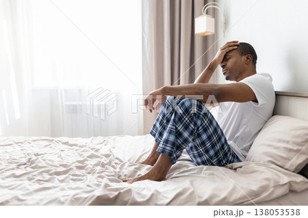 Young black man sitting on bed holding head in pain, looking stressed Young black man sitting on bed holding head in pain, looking stressed 138053538