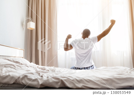 Young african american man stretching arms energetically on bed after waking up Young african american man stretching arms energetically on bed after waking up 138053549