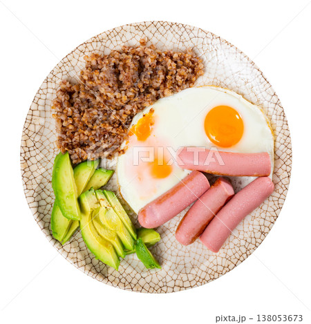 Two fried eggs, sausages, boiled buckwheat, and half avocado sliced into wedges. Two fried eggs, sausages, boiled buckwheat, and half avocado sliced into wedges. 138053673