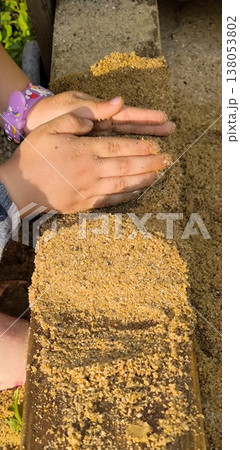 Children's hands playing with sand on a wooden surface 138053802