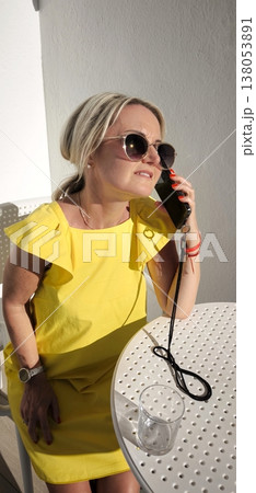 Blonde woman in yellow dress talking on phone outdoors 138053891