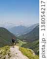 Hiker walking down steep alpine trail overlooking valley, French Alps 138054217