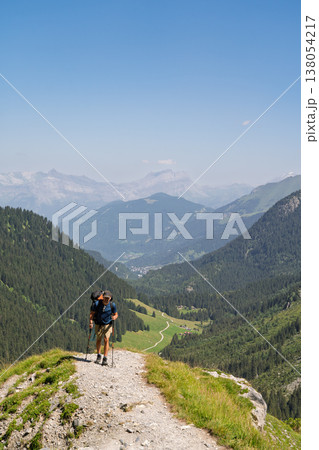 Hiker walking down steep alpine trail overlooking valley, French Alps Hiker walking down steep alpine trail overlooking valley, French Alps 138054217