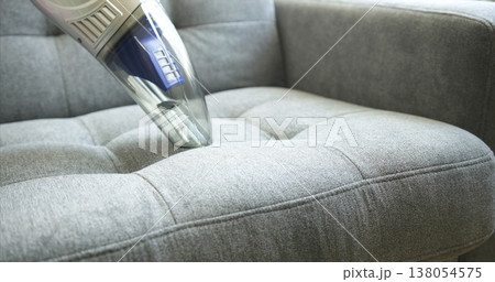 Vacuuming a gray couch during house cleaning in the living room with a handheld vacuum cleaner Vacuuming a gray couch during house cleaning in the living room with a handheld vacuum cleaner 138054575