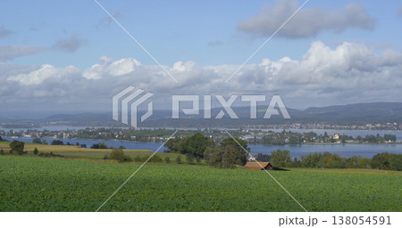 View of a lake surrounded by hills and clouds near a small town in the daytime hours of early fall 138054591