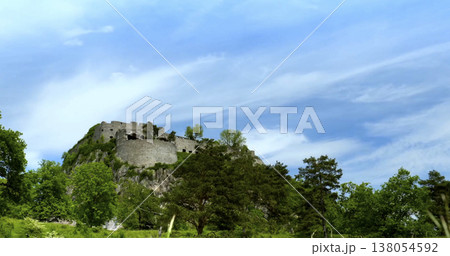 Castle sits on a hill under a blue sky surrounded by green trees in a rural setting with scattered clouds in the background 138054592