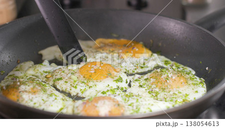 Cooking eggs in a frying pan with herbs and spices for breakfast in a kitchen setting 138054613